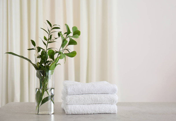 Verse handdoeken en groene takken op lichtgrijze stenen tafel in de badkamer - Foto, afbeelding