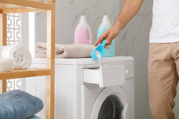 Man pouring laundry detergent into washing machine drawer in bathroom, closeup - Fotó, kép