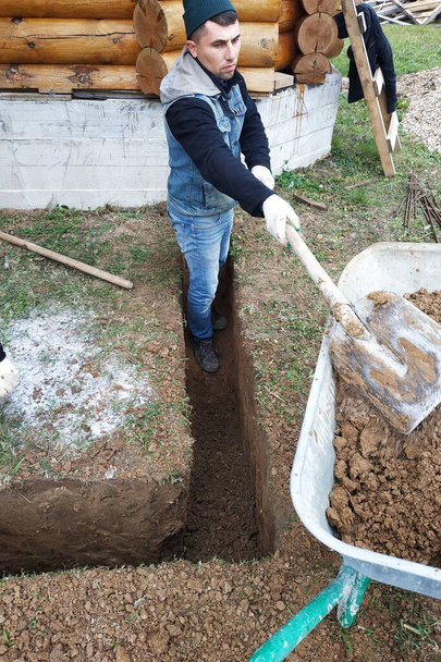 Työntekijä kaivaa kaivannon lapion lähelle taloa.2020 - Valokuva, kuva