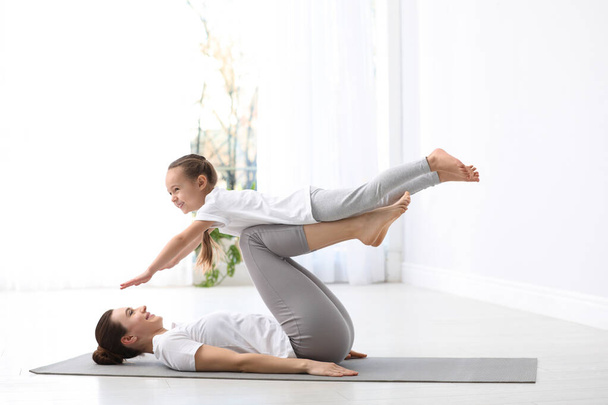 Young mother with little daughter practicing yoga at home - Фото, зображення