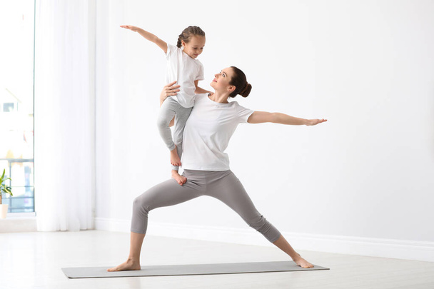 Young mother with little daughter practicing yoga at home - Foto, afbeelding