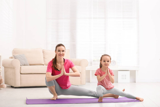 Young mother with little daughter practicing yoga at home - Fotoğraf, Görsel