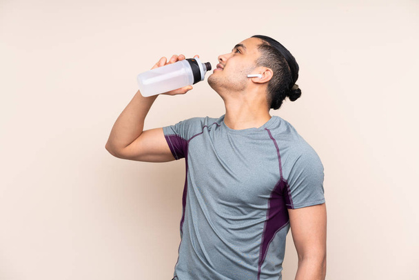 Asiatischer Sportler isoliert auf beigem Hintergrund mit Sportwasserflasche - Foto, Bild