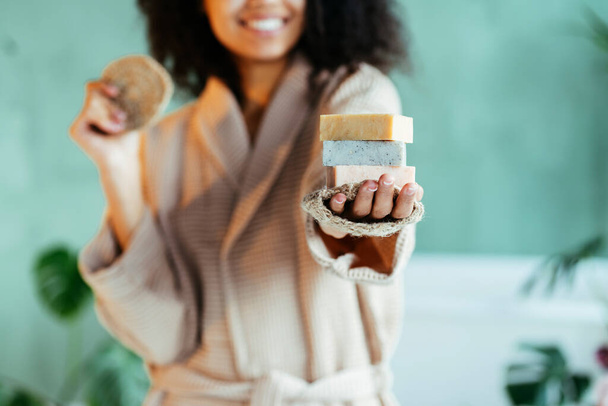 Primer plano de la mujer afroamericana multiétnica que le muestra tres jabón aromaterapia natural hecha a mano para el bien de su vida. Enfoque selectivo. Interior verde moderno
. - Foto, Imagen