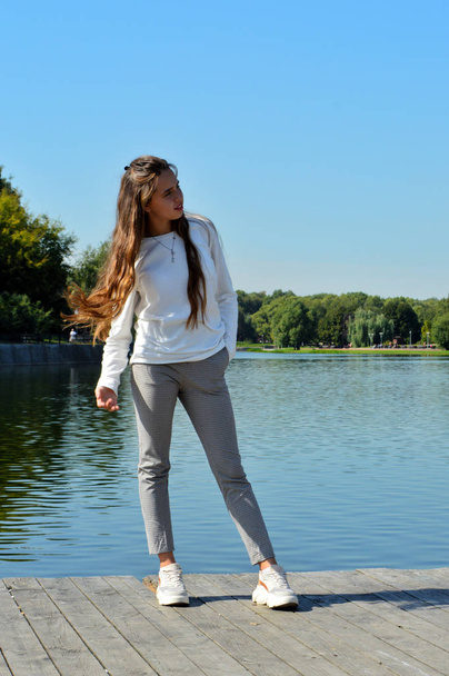 Een jong meisje op een houten pier bij het water - Foto, afbeelding