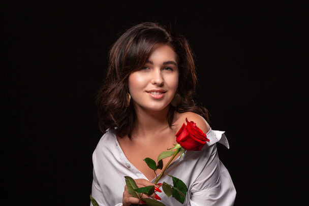 Beautiful woman with bright makeup posing isolated over black background with red rose.  - 写真・画像