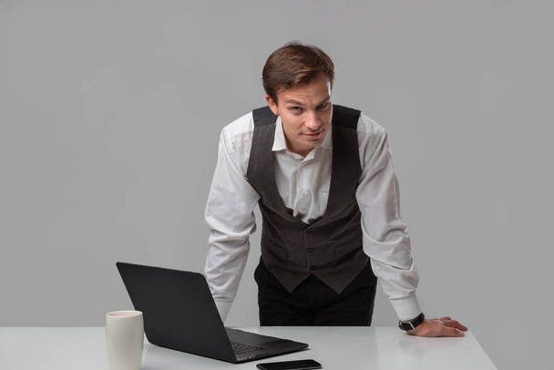 Zakenman in wit t-shirt en grijs vest aan het werk op laptop - Foto, afbeelding