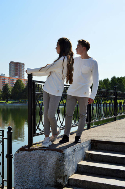 Een jong meisje en een jonge man in dezelfde kleren op een brug bij het water - Foto, afbeelding