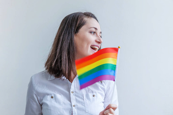 白地にLGBTの虹の旗が描かれた美しい白人レズビアンの女の子は幸せそして興奮しています。若い女性ゲイの誇りの肖像画。lgbtqコミュニティの概念に対する平等な権利 - 写真・画像