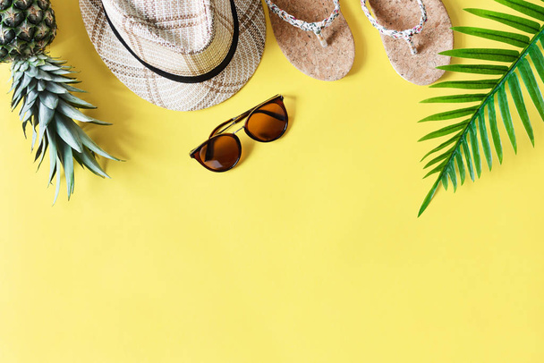 Красочная летняя композиция с соломенной шляпой, солнцезащитными очками, пальмовым ветром, ананасами и шлепанцами на желтом фоне сверху. Летняя мода, концепция отдыха
. - Фото, изображение