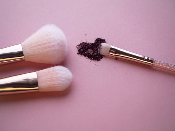 Καλλυντικά nylon πινέλα μακιγιάζ σε ροζ φόντο με θρυμματισμένο δαμάσκηνο shimmer σκιές ματιών για smokey επίδραση πάγου. Βάση, σκόνη και ρουζ βούρτσα σκιά ματιών. Επαγγελματικά εξαρτήματα μακιγιάζ. - Φωτογραφία, εικόνα