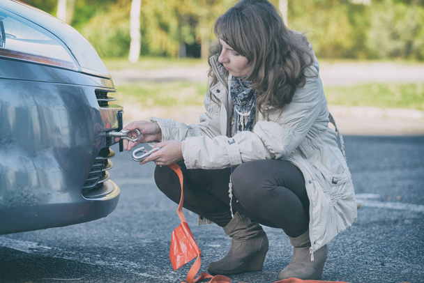Belle femme assemblant crochet de remorquage à une voiture cassée et tenant la corde de remorquage dans l'autre main
 - Photo, image