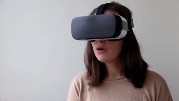 Sonríe mujer joven usando realidad virtual gafas VR casco auriculares sobre fondo blanco. Smartphone con gafas de realidad virtual. Tecnología, simulación, alta tecnología, concepto de videojuego - Imágenes, Vídeo