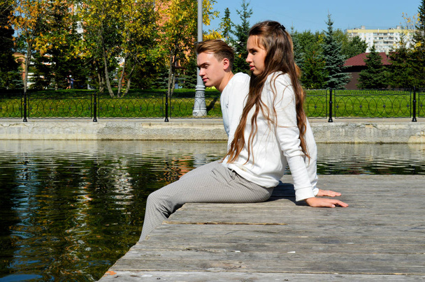 Een jong meisje en een jonge man in dezelfde kleding op een houten pier bij het water - Foto, afbeelding