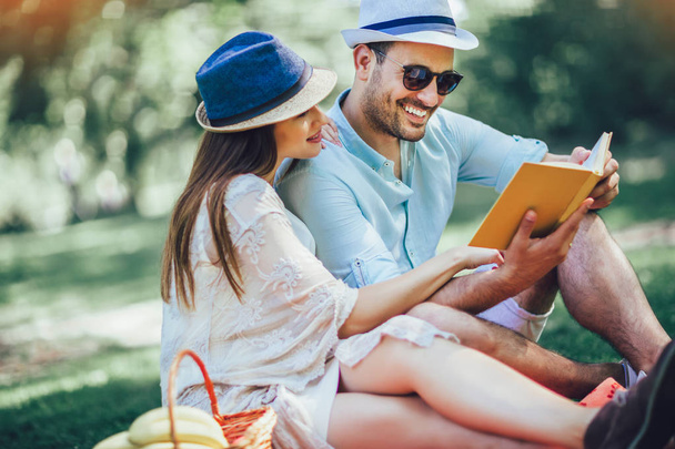 Beautiful couple enjoying picnic time outdoor reading book - Fotoğraf, Görsel