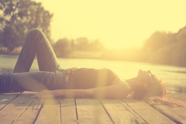 湖の夕日で木製の桟橋にリラックスした若い女性のビンテージ写真 - 写真・画像