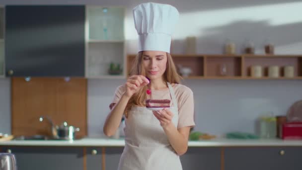 Konditor dekoriert Kuchen mit Kirsche am Arbeitsplatz. Frau blickt in Kamera - Filmmaterial, Video
