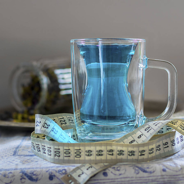 Butterfly pea flower blue tea in glass mug with silhouette like slim woman figure. With measuring tape around as drink helps to loose weight. Square. Healthy thai detox herbal beverage. - Foto, Bild