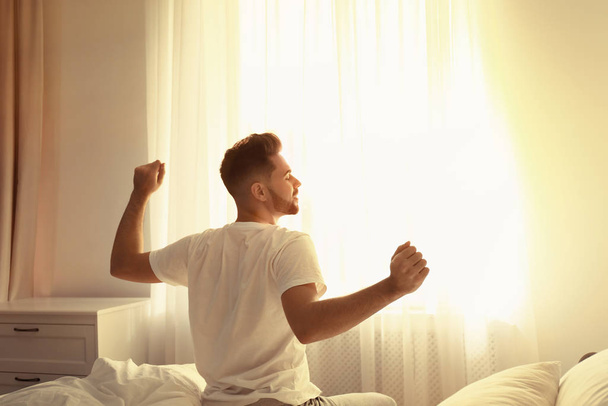 若い男が家でベッドの上で、後ろからの眺めストレッチ。ゆっくり朝 - 写真・画像
