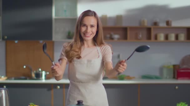 Vrouw met lepels in de hand in de keuken. Vrouw op zoek naar camera op keuken - Video