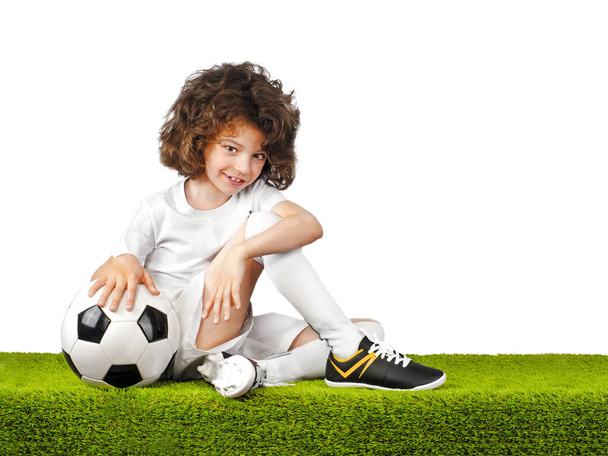 A young football player with a ball sits on the grass of the stadium. - Foto, Imagem