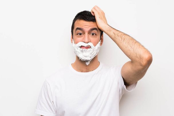 Mann rasiert sich seinen Bart vor isoliertem weißen Hintergrund mit einem Ausdruck der Frustration und des Unverständnisses - Foto, Bild