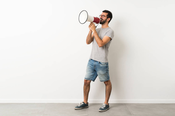A full-length shot of handsome man with beard shouting through a megaphone - Photo, Image
