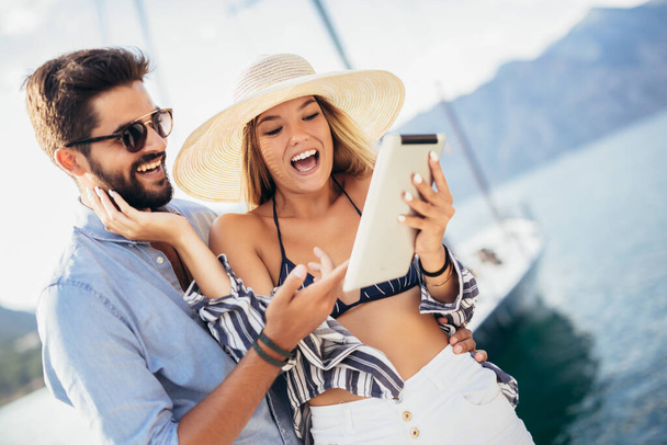 観光の海のリゾートのデジタルタブレットを使用して港のそばを歩く幸せな若いカップル - 写真・画像