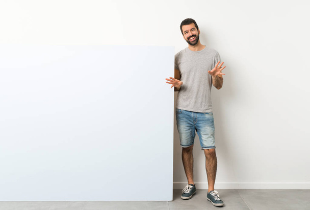 Young handsome man with beard holding a big blue empty placard smiling - Fotoğraf, Görsel