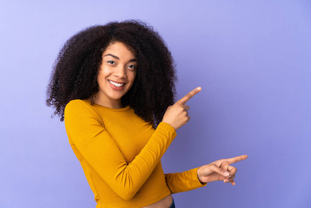 Mladá africká americká žena izolovaná na fialovém pozadí ukazující prstem na stranu a prezentující produkt - Fotografie, Obrázek