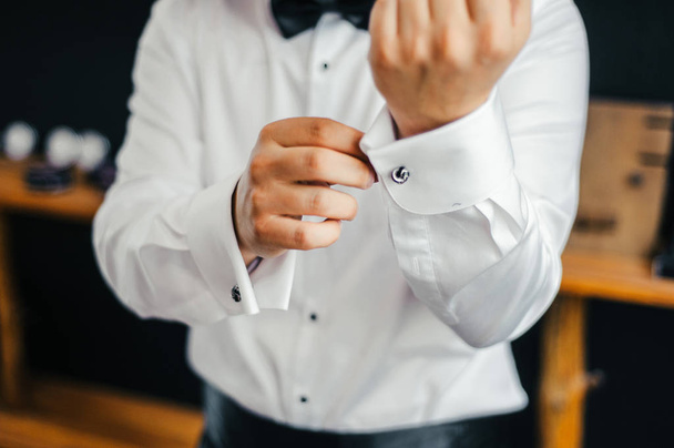 noivo em uma camisa branca e gravata arco prende seus abotoaduras nas mangas
 - Foto, Imagem