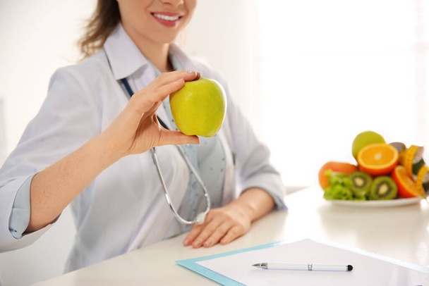 Nutritionist with apple at desk in office, closeup. Space for text - Fotoğraf, Görsel
