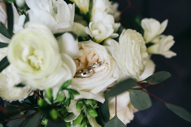 Beyaz güllerin ve yeşilliklerin düğün çiçekleri; çiçeklerden birinde beyaz altın alyanslar var. - Fotoğraf, Görsel