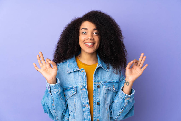 Mladý africký americký žena izolovaný na fialové pozadí ukazující ok znamení se dvěma rukama - Fotografie, Obrázek