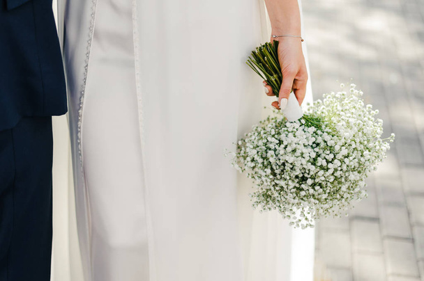 The bride is holding a wedding bouquet of white flowers. The bride stands on the street in the city - Fotó, kép