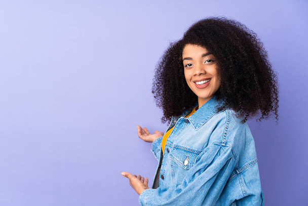 Young african american woman isolated on purple background extending hands to the side for inviting to come - Foto, Imagem