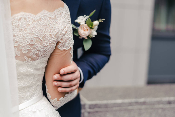 groom in a dark blue suit with a boutonniere holding the hand of a bride in a white lace dress and veil - Foto, immagini