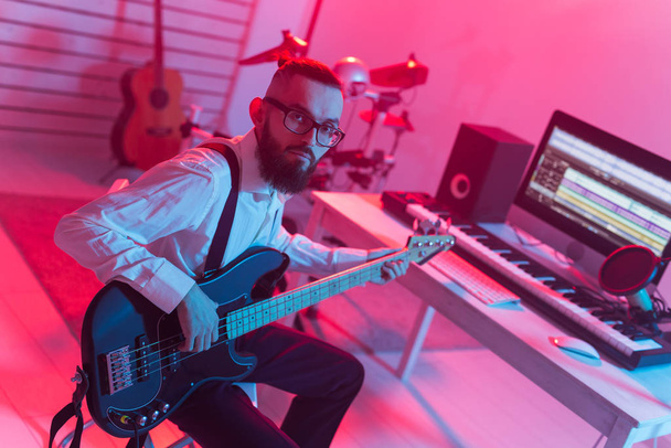 Create music and a recording studio concept - Bearded funny man guitarist recording electric guitar track in home studio - Zdjęcie, obraz
