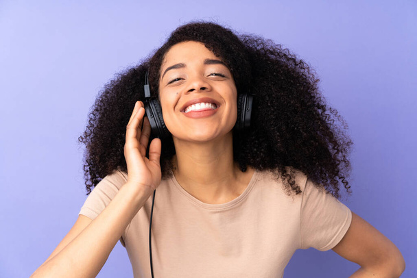 Genç Afrikalı Amerikalı kadın, mor arka planda izole edilmiş müzik dinliyor. - Fotoğraf, Görsel