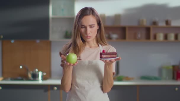 Woman making choice between apple and cake on kitchen. Woman choosing apple - Video