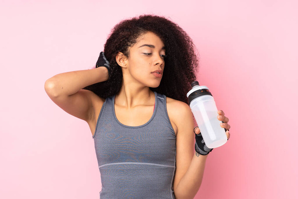Young african american sport woman isolated on pink background with sports water bottle - Zdjęcie, obraz