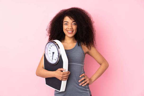 Young african american woman isolated on pink background with weighing machine - Photo, Image