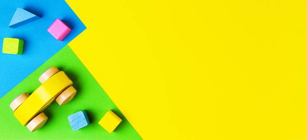 Macchina giocattolo in legno rosso con blocchi colorati su sfondo geometrico giallo blu verde. Vista dall'alto
 - Foto, immagini