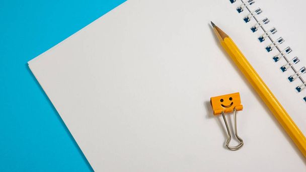 Zápisník s tužkami a žluté a modré pojivo klipu na modrém pozadí - Fotografie, Obrázek