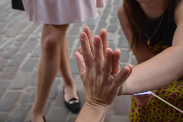Две женщины сжимают руки вместе с выровненными пальцами. Ноги другой девушки на заднем плане
. - Фото, изображение