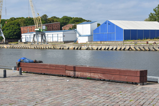 Uitzicht op de haven kanaal met dronken man slapen op bank - Foto, afbeelding