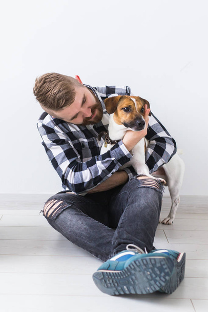 Pets owner concept - Attractive cheerful male in plaid shirt holds favourite pet. Happy bearded man with his jack russell terrier - Zdjęcie, obraz