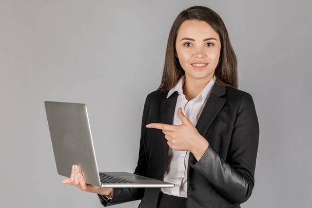 Jeune femme d'affaires dans une suite sombre avec ordinateur portable sur fond gris. Concept de bureau - Photo, image