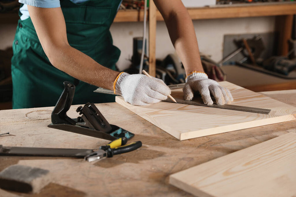 Professional carpenter measuring wooden board in workshop, closeup - Фото, изображение