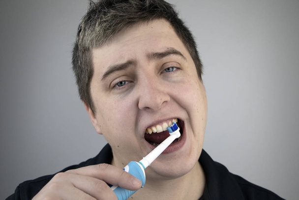 Uykulu adam dişlerini elektrikli fırçayla fırçalar. Ağız temizliği kavramı. Yorgun adam dişleriyle ilgileniyor. - Fotoğraf, Görsel